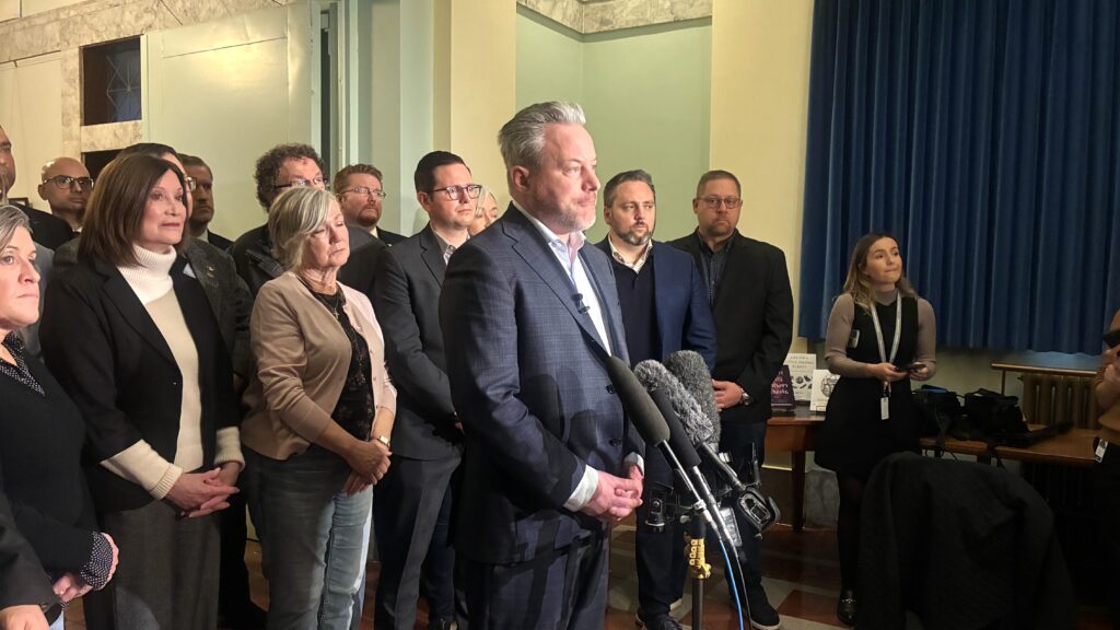 Trevor Halford addresses media with caucus members standing behind him